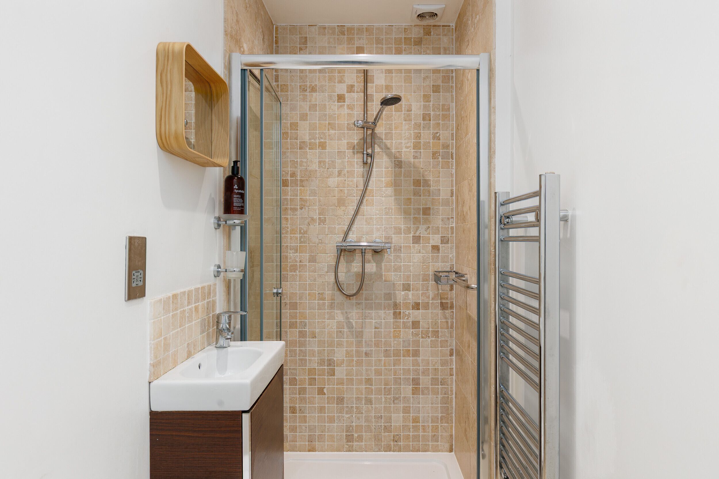 Een douche met glazen deur, een wastafel en een houten plank.