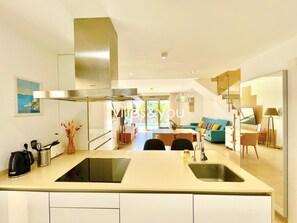 Une cuisine moderne dotée d’un îlot central, un coin repas avec un canapé et une table, et un escalier menant à un autre niveau.