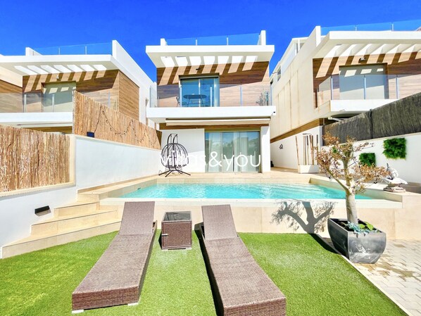 Une maison moderne à deux étages, dotée d’une piscine, d’un espace extérieur aménagé et d’un panneau indiquant « et vous ».