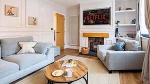 A living room with two grey sofas, a coffee table with a magazine and a cup, a fireplace, and a large Netflix poster on the wall.