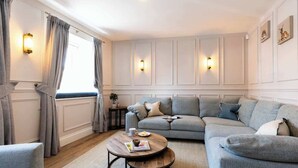 A living room with a grey sofa, a round coffee table, and a window with curtains.