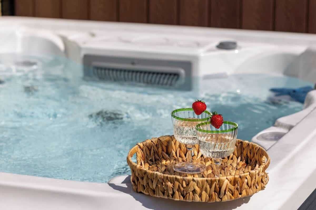 A hot tub with two glasses of water and strawberries on a woven tray.
