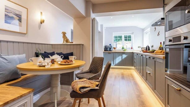 A modern kitchen with grey cabinets, a built-in oven, and a dining area with a round table and two chairs.