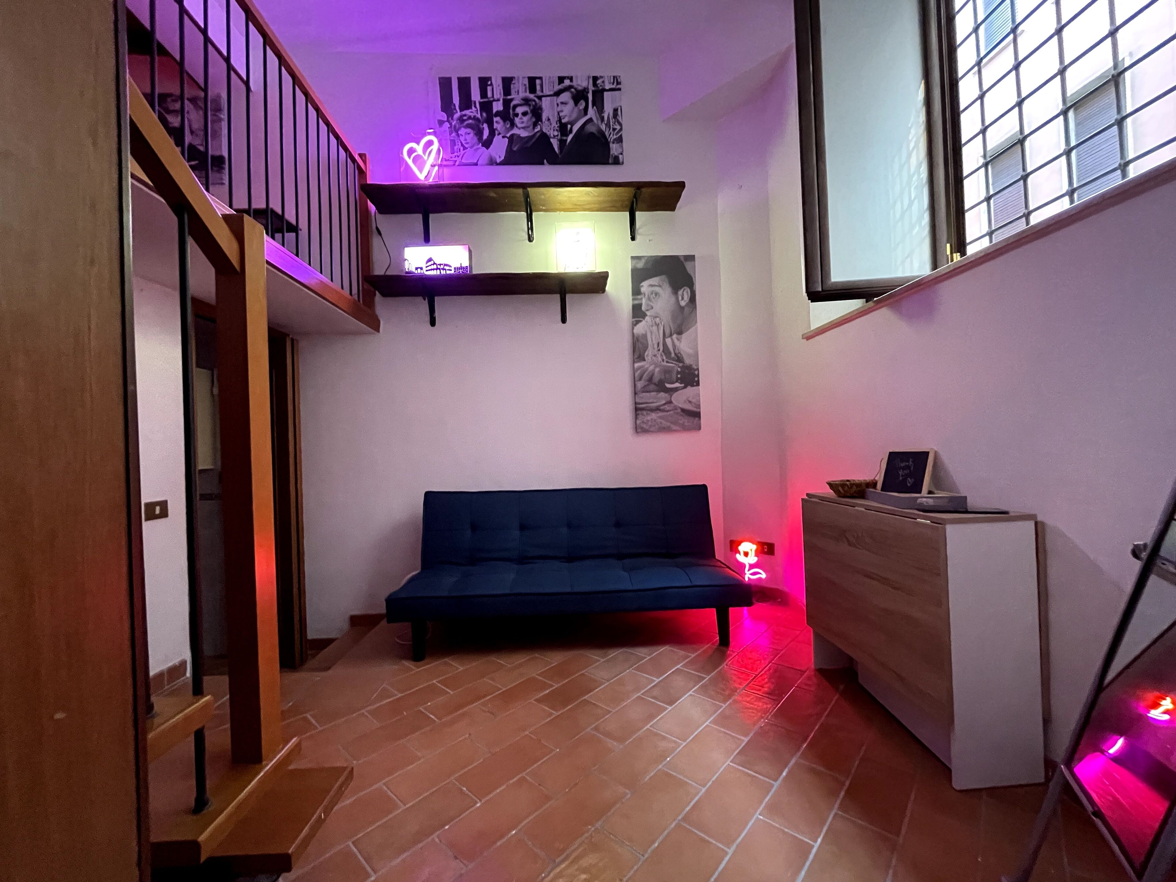 Una habitació amb un sofà, un armari de fusta, una escala i una decoració de cor de neó.