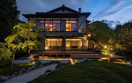 A modern two-story house with a large deck, surrounded by a well-maintained garden with rocks and trees.