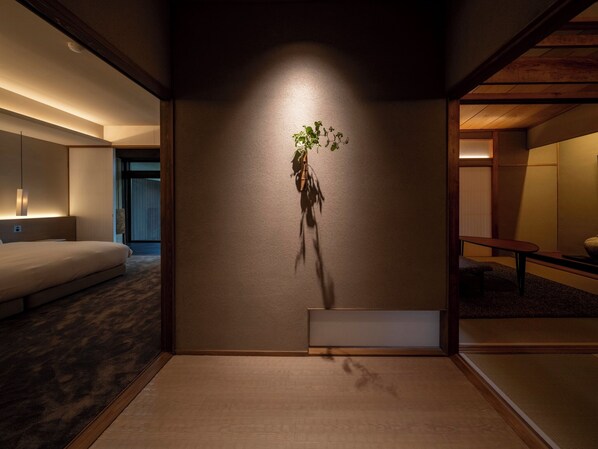 A modern hotel room with a large bed, a bedside table, a wall-mounted plant, and a sliding door leading to another room.