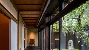 A corridor with dark wooden flooring, large windows, and a view of a garden with a stone monument. - Momoyama Onsen Tsukimikan (Kyoto)