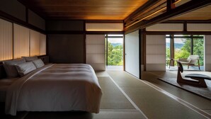 A traditional Japanese-style bedroom with tatami flooring, a large bed, sliding shoji doors, and a view of a mountainous landscape. - Momoyama Onsen Tsukimikan (Kyoto)