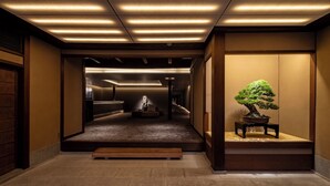 A hallway with a wooden bench, a bonsai tree, and a statue. - Momoyama Onsen Tsukimikan (Kyoto)