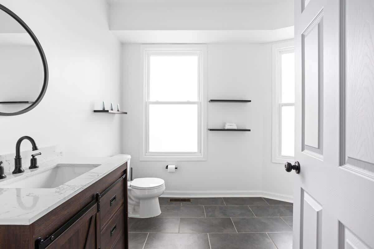 Une salle de bain moderne avec un meuble-lavabo blanc, un évier, des toilettes et une fenêtre.
