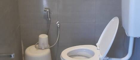 A small, enclosed bathroom with a toilet, a bidet, and a handrail.