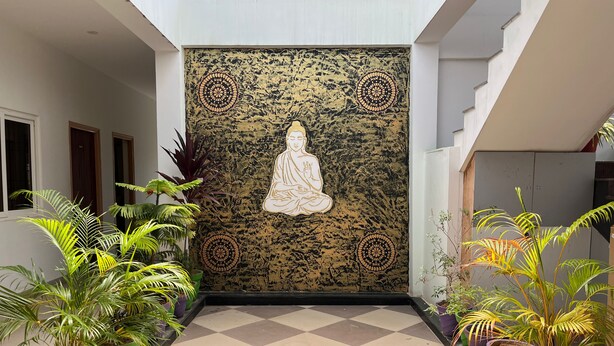 Un pasillo con un papel tapiz decorado, una estatua serena y plantas en macetas.