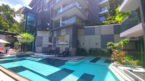 Un hotel moderno con piscina, sillones de descanso y sombrillas exteriores.
