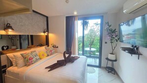 Habitación de hotel con cama, televisión, balcón con mesa y sillas, y planta en maceta.