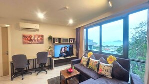 Una sala de estar moderna con un ventanal grande, un sofá con cojines decorativos, un televisor y un escritorio con dos sillas.