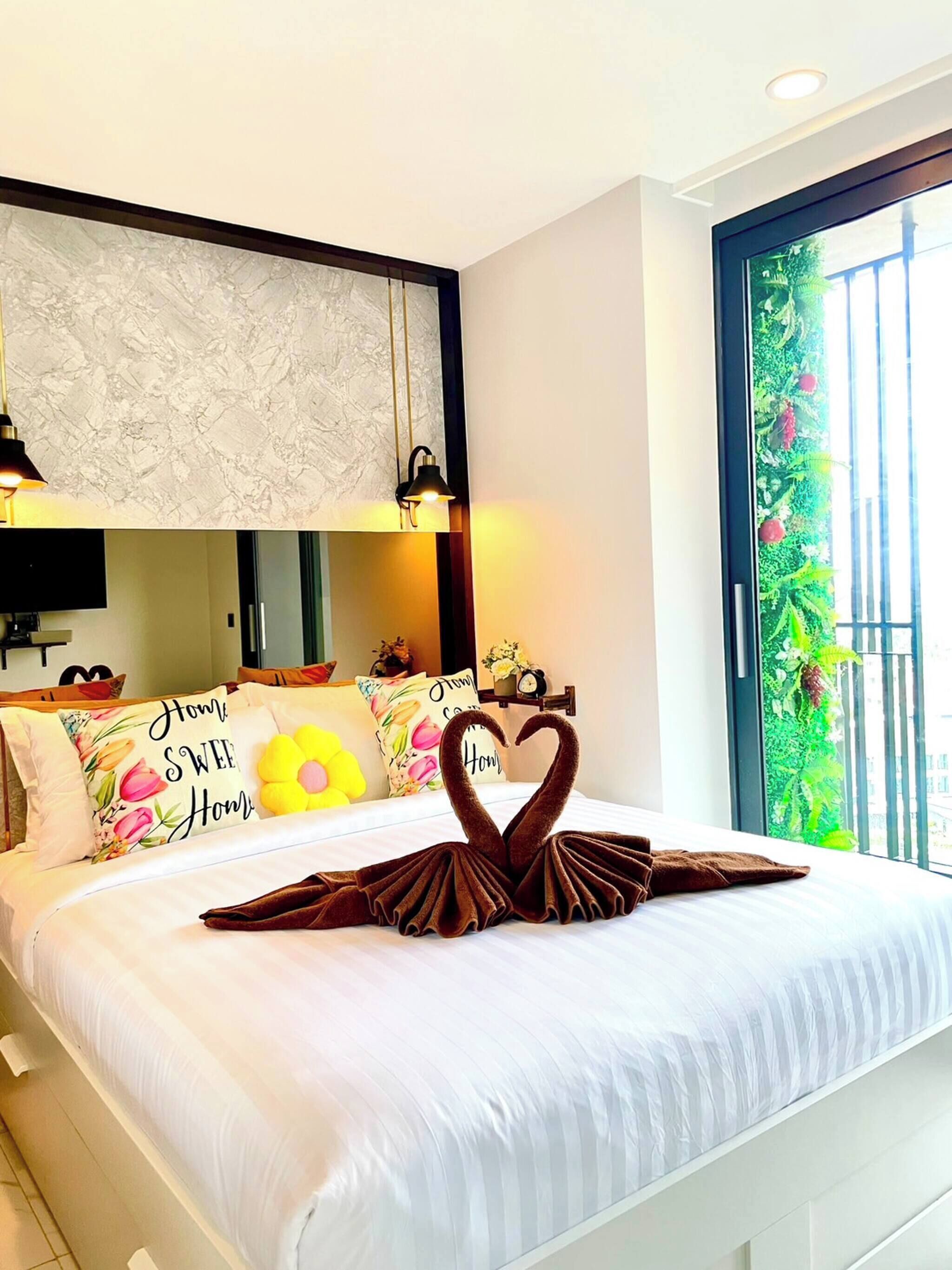A hotel room with a neatly made bed, a large window with a view of greenery, and a wall-mounted TV.