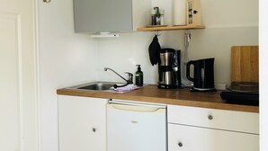 A compact kitchen with white cabinets, a built-in dishwasher, a wooden countertop, and a coffee maker. - Tower room in the Pilsumer Hof (Krummhörn)