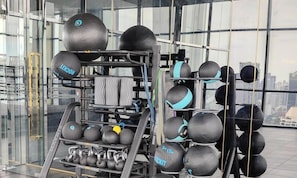 Une salle de sport Ă©quipĂ©e de divers appareils dâentraĂźnement, notamment des kettlebells, des balles lestĂ©es et un support Ă squats.