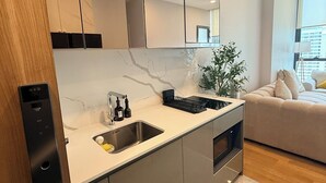Uma cozinha moderna com uma pia embutida, um espelho sobre o balcão e vista para a sala de estar, com um sofá e uma planta.