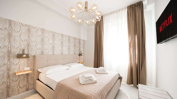 A modern hotel room with a large bed, a wall-mounted TV, and a ceiling light fixture. - Avenue Suites (Bologna)
