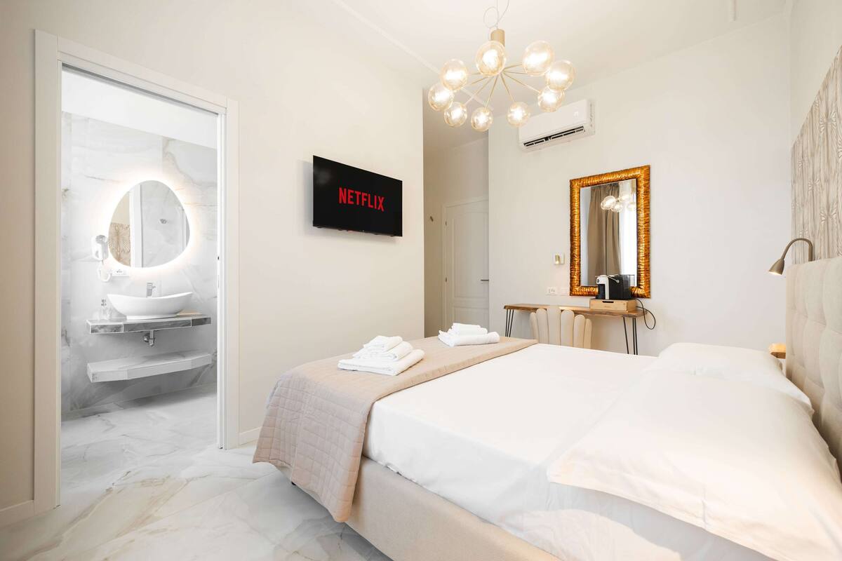 Moderni hotellihuone, jossa on suuri sänky, peilillä varustettu meikkipöytä, televisio ja kattokruunu.
