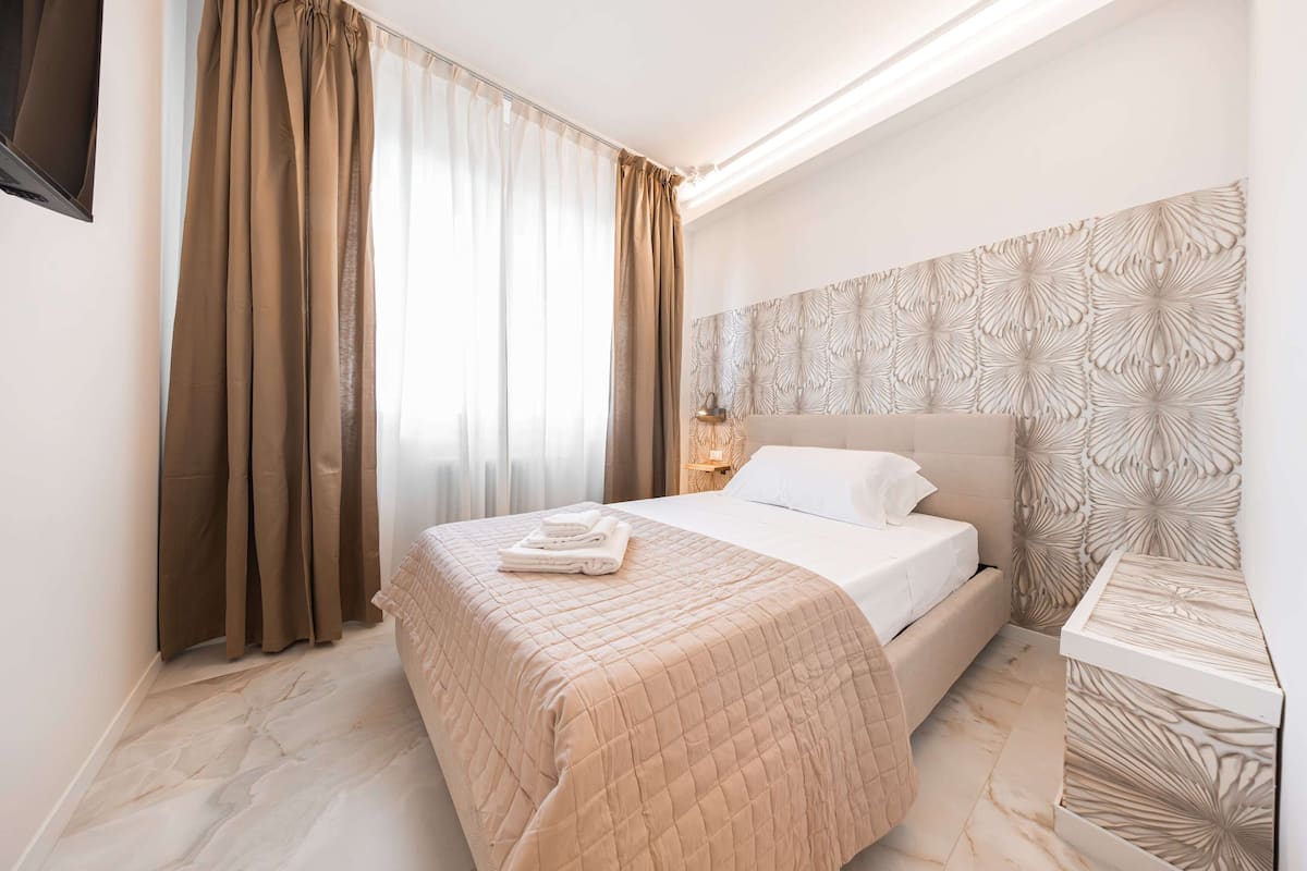 Hotellihuone, jossa on sänky, yöpöytä, lamppu ja koristeellinen seinäpaneeli.