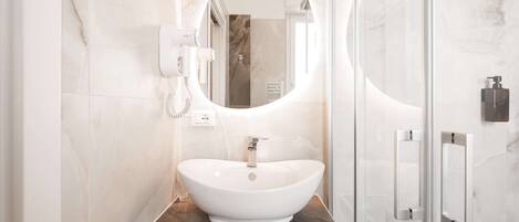Un baño moderno con un espejo ovalado grande, un lavamanos blanco tipo recipiente y una pared revestida de mármol.