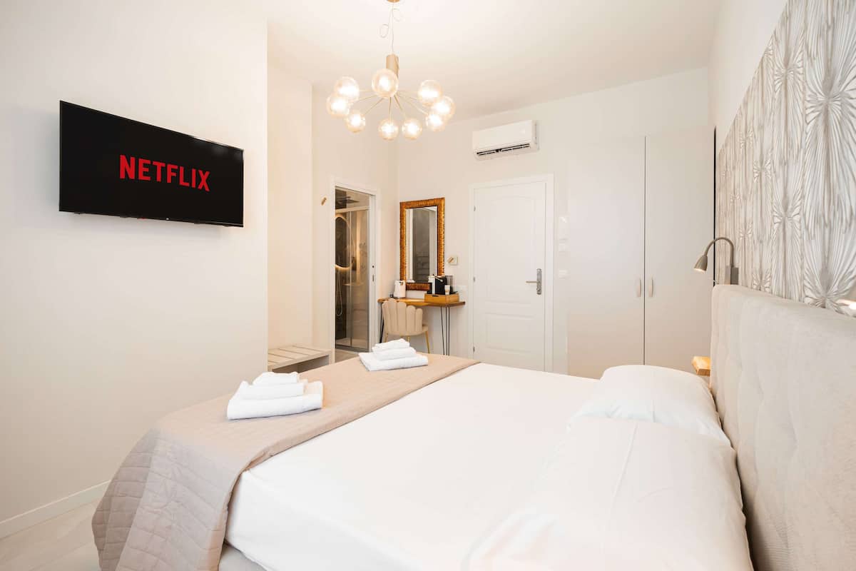 Hotellihuone, jossa on sänky, televisio, jossa näkyy Netflixin logo, peili ja ovi.