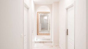A hallway with white walls and a marble floor, leading to a mirrored door frame. - Avenue Suites (Bologna)
