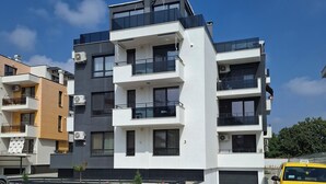 A multi-story residential building with balconies, a parking area, and a yellow car parked in front.