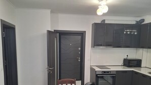 A dining area with a round wooden table and four chairs, a dark door, and a kitchen with modern appliances.
