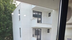 A modern building with a glass balcony, a visible air conditioning unit, and a window with a black frame.