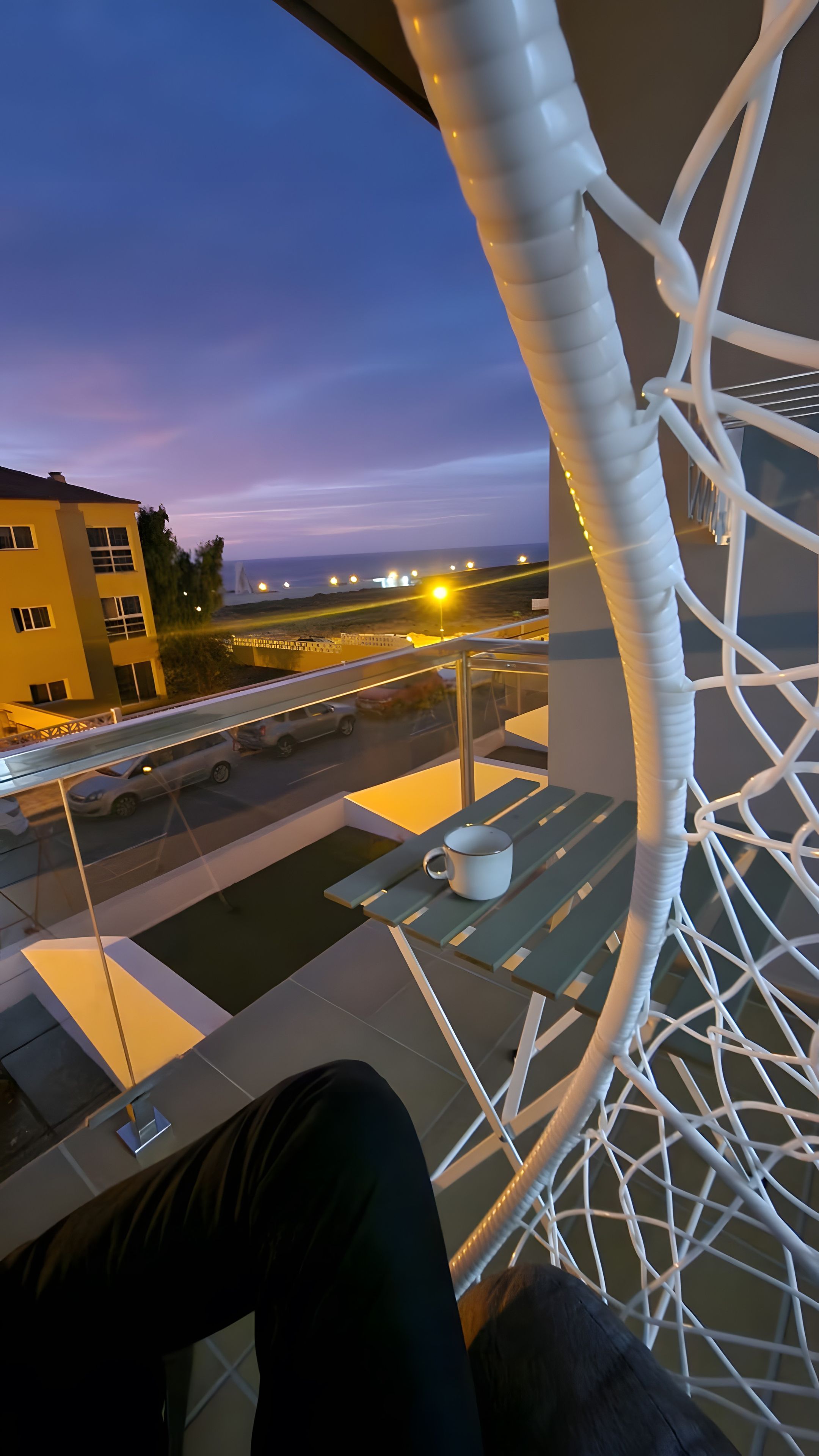 Un balcon doté d’une structure en treillis blanc, une table avec une tasse, et une vue sur une route où circulent des véhicules.