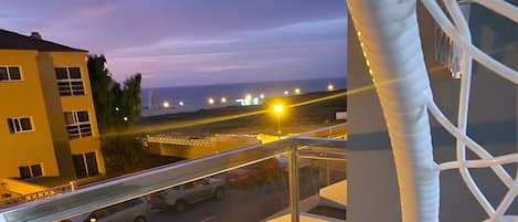 A balcony with a white net structure, a table with a cup, and a view of a road with vehicles.