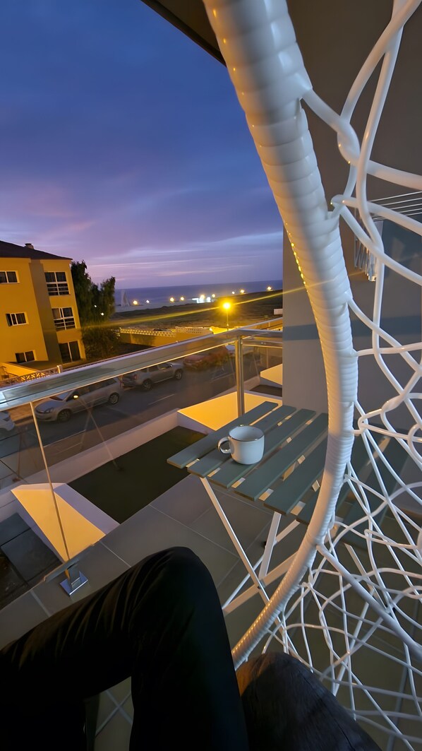 Un balcon doté d’une structure en treillis blanc, une table avec une tasse, et une vue sur une route où circulent des véhicules.
