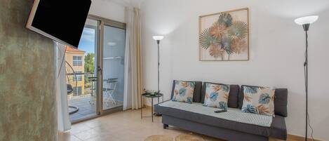 A modern living room with a sofa, a flat-screen TV, a floor lamp, and a decorative wall piece.