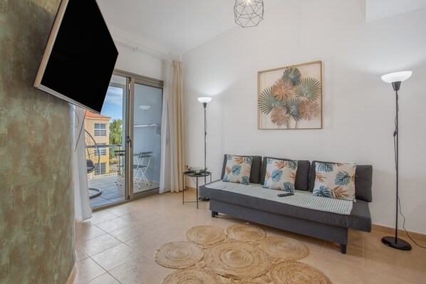 A modern living room with a sofa, a flat-screen TV, a floor lamp, and a decorative wall piece.