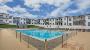 Una piscina con sillas de descanso y sombrillas, rodeada de edificios de varios pisos con balcones.