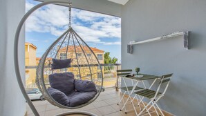 Un balcón con una silla colgante, una pequeña mesa con sillas y vistas a edificios.