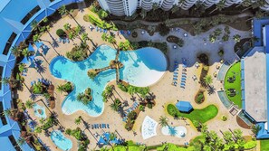 An aerial view of a resort with multiple swimming pools, sun loungers, and palm trees. - Coastal Haven: Heated Pools with a Beach Shuttle! (Destin)