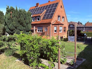 Ein Haus mit Solaranlage, Backsteinfassade und einem Garten mit verschiedenen Pflanzen.