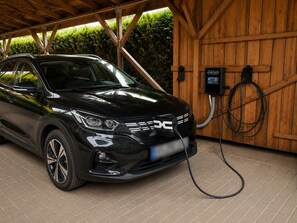 A black SUV parked under a wooden structure with a charging station.