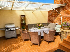An outdoor patio with a grill, wicker furniture, a table with a vase of flowers, and a brick wall.