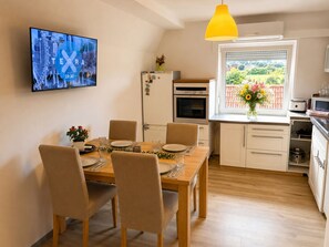 A dining area with a wooden table set for four, a television mounted on the wall, a refrigerator, and a window with a view of greenery. - *SilentSun.net* - peace and relaxation 2.5 bedrooms, large kitchen and bathroom (Gudow)