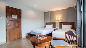 A hotel room with two beds, a wooden door, a small table with a magazine, and a chair. - Carunda Hotel Pattaya (Sattahip)