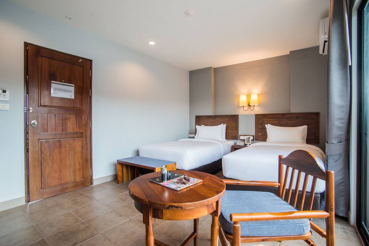 Une chambre d’hôtel avec deux lits, une porte en bois, une petite table avec un magazine et une chaise.