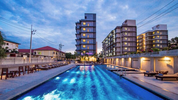 A swimming pool with lounge chairs and a building with multiple floors and balconies. - Carunda Hotel Pattaya (Sattahip)