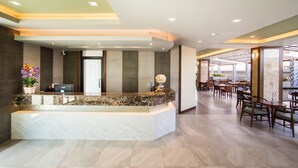 A hotel reception area with a marble counter, seating area, and large windows. - Carunda Hotel Pattaya (Sattahip)