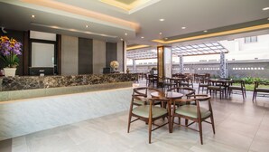 A modern hotel lobby with marble reception counters, wooden chairs, and a large glass window overlooking the street. - Carunda Hotel Pattaya (Sattahip)