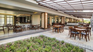 A spacious outdoor dining area with multiple tables and chairs, a covered walkway, and a garden with potted plants. - Carunda Hotel Pattaya (Sattahip)